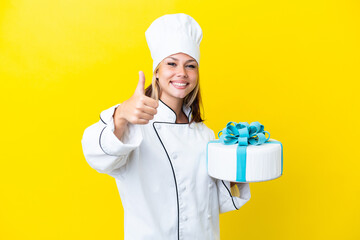 Young Russian pastry chef woman with a big cake isolated on yellow background with thumbs up because something good has happened