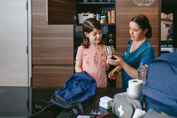 Mother preparing emergency backpack with her daughter in the kitchen
