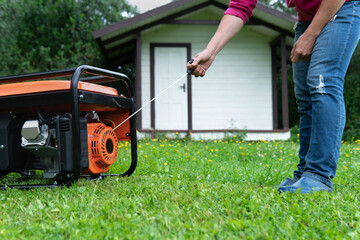 Woman starts a portable electric generator standing on the grass on the backyard of a summer house...