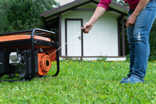 Woman starts a portable electric generator standing on the grass on the backyard of a summer house in summer evening