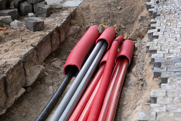 A large number of electric and high-speed Internet Network cables in red corrugated pipe are buried underground on the street covered with cobblestones.  - obrazy, fototapety, plakaty