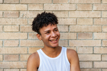 Afro latin male teenager smiling against a wall