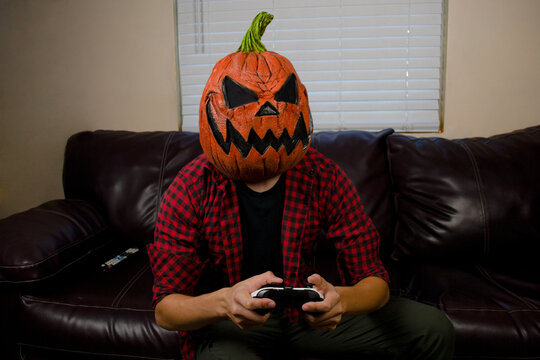 Scary Halloween pumpkin man playing video games in the living room.  Jack o lantern man