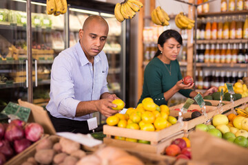 Portrait of latin american man shopping in food store, choosing ripe sweet mandarines
