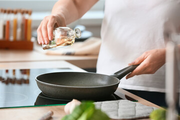 Mature woman pouring oil into frying pan in kitchen