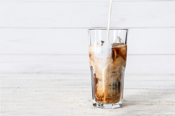 Pouring of milk into glass with tasty iced coffee on table