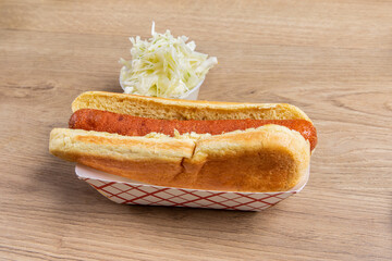 A plain hotdog in a bun with coleslaw or sauerkraut on a wooden table