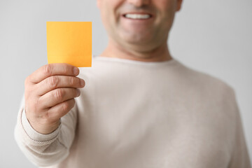 Mature man with blank note paper sheet on light background, closeup