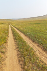 Fototapeta na wymiar Dirt road on sandy soil in the steppe with green meadows on Olkhon island, Siberian Baikal Lake. Summer landscape. Travel and long distance path concept