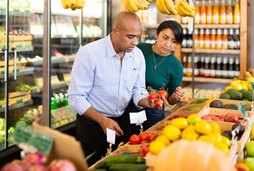 Obraz premium Married couple choosing ripe tomatoes at grocery store