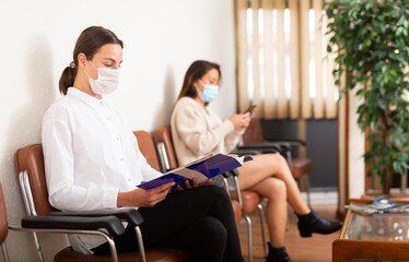 Portrait of woman in face mask sitting at hall in office, waiting for business meeting during coronavirus pandemic