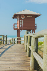 Wooden boardwalk on the beach with lifeguard tower on an empty beach with clear sand and blue sea in southern Brazil. Lifeguard station. Safety concept.