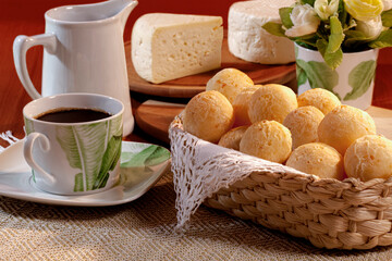 Pão de queijo na cesta com café e pedaço de queijo em mesa decorada.