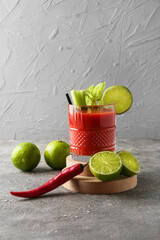 Glass of bloody mary cocktail, red chili pepper and limes on grunge background