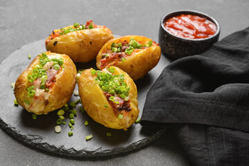 Slate plate with baked potato and sauce on dark background