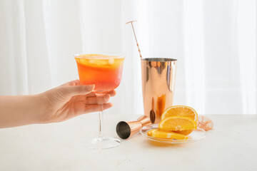 Female hand with glass of Aperol spritz cocktail on light background