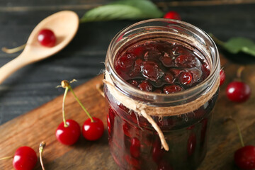 Jar with tasty cherry jam on dark wooden background, closeup