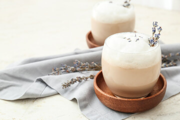 Glasses of tasty lavender latte and flowers on light background