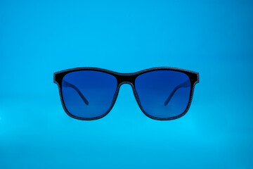 Sun Glasses with blue glass and black frame on blue background