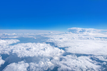Top view from the airplane window on beautiful cumulus fluffy white clouds on a blue sky with a bright sun. Perfect abstract sky background, wallpaper, layout.