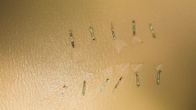 Multiple fishermen in bright colorful boars working as a team to catch a shoal of fish.  Cast net synchronized on open lake in Southeast Asia, birdseye view.