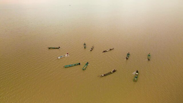 Multiple fishermen in bright colorful boars working as a team gathering their fishing nets.  Cast net synchronized on open lake in Southeast Asia, drone view.