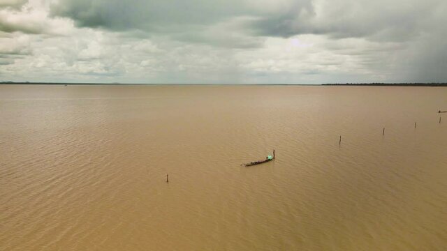 Fisherman in boat attending to his nets in wide open muddy lake with view of horizon.