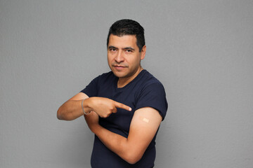 Happy Latino adult man shows his arm that just received the Covid-19 vaccine in the new normal for...