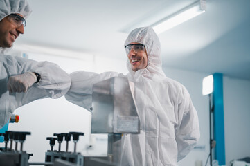 Two scientists wearing uniform protection. Check the manufacturing process face masks. With machinery in a laboratory at industry plants. The concept for security and protection coronavirus covid-19.