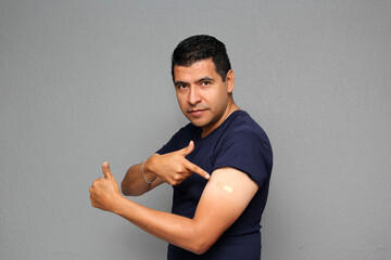 Happy Latino adult man shows his arm that just received the Covid-19 vaccine in the new normal for...