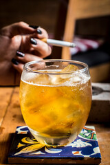 yellow cocktail drink with ice and background of hand with cigar