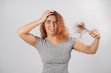 Caucasian woman with a grimace of horror holds a comb with a bun of hair. Hair loss and female...