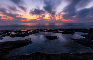 amazing scenic view at a sea shore from a coast after dramatic colorful sunset with flying blured clouds and reflection on water surface , beautiful ocean landscape