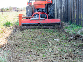 a tractor with a mower attached mulches dry grass along the fence. Land plot processing