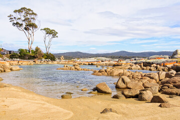 Little pond in Skeleton Bay surrounded by boulders draped in orange lichen - Binalong Bay,...