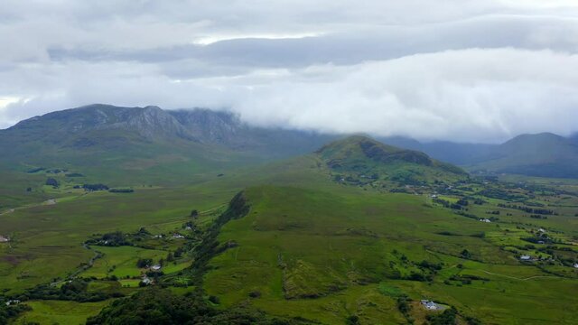 Maumturk Mountains, Maum, Connemara, County Galway, Ireland, July 2021. Drone gradually descends while facing west towards rugged cloud swept hills with rural cottages and grassy marshland.