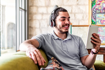 Happy man using a tablet to watch online content sitting on a couch at home.