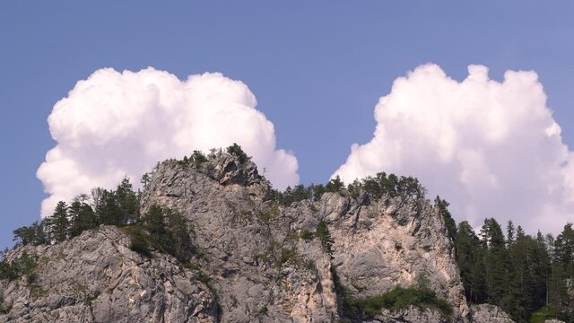 Close up shot of beautiful cliffs with high clouds and few trees on clear blue sky day