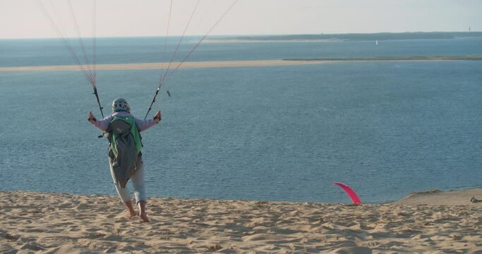 Back View Of A Paraglider Ready To Fly On The Sand Dune At The Sea Coast In Summer. wide shot