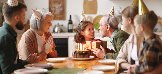 Loving senior  man giving gift to excited happy granddaughter during Birthday celebration with family