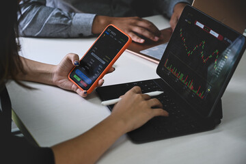 Businesswoman using smart phone and analyzing investment charts with computer tablet.