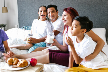 Hispanic teenage girl with cerebral palsy and her family having breakfast on bed at home, in...