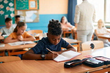 African American elementary student writes during class at school.