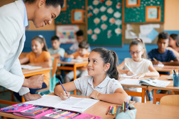 Happy schoolgirl talks to teacher while learning in classroom at elementary school.