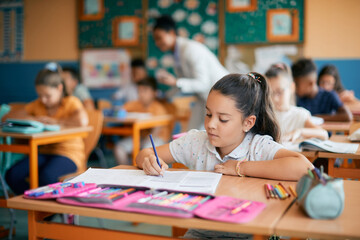 Little girl writes in notebook while having class at elementary school.