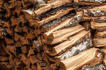 Birch firewood with bark outdoors. Oven-wood for the stove is stacked in woodpiles. Fuel for country life. The rough texture of natural wood.