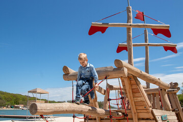 Naklejka na ściany i meble A boy is playing on a wooden playground in the form of a ship. Afternoon walk. Selective focus.