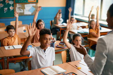 Multi-ethnic group of elementary students raise their hands to answer question during class at school. - obrazy, fototapety, plakaty
