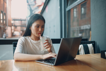 Fototapeta na wymiar Asian young woman drink lemonade soda and using laptop at the outdoors cafe.