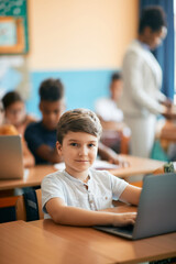 Smiling schoolboy e-learns on laptop during computer class at elementary school.